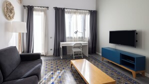 A modern living room with a sofa, a wooden coffee table, a desk with a chair, a TV, and a blue entertainment unit. - Stay U-nique Apartments at Av. Republica Argentina (Barcelona)