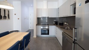 A modern kitchen with white cabinets, stainless steel appliances, a wooden dining table, and blue chairs. - Stay U-nique Apartments at Av. Republica Argentina (Barcelona)