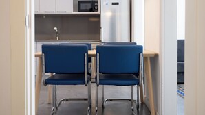 A small kitchenette with a microwave, refrigerator, and sink. There are two blue chairs and a table in the foreground. - Stay U-nique Apartments at Av. Republica Argentina (Barcelona)
