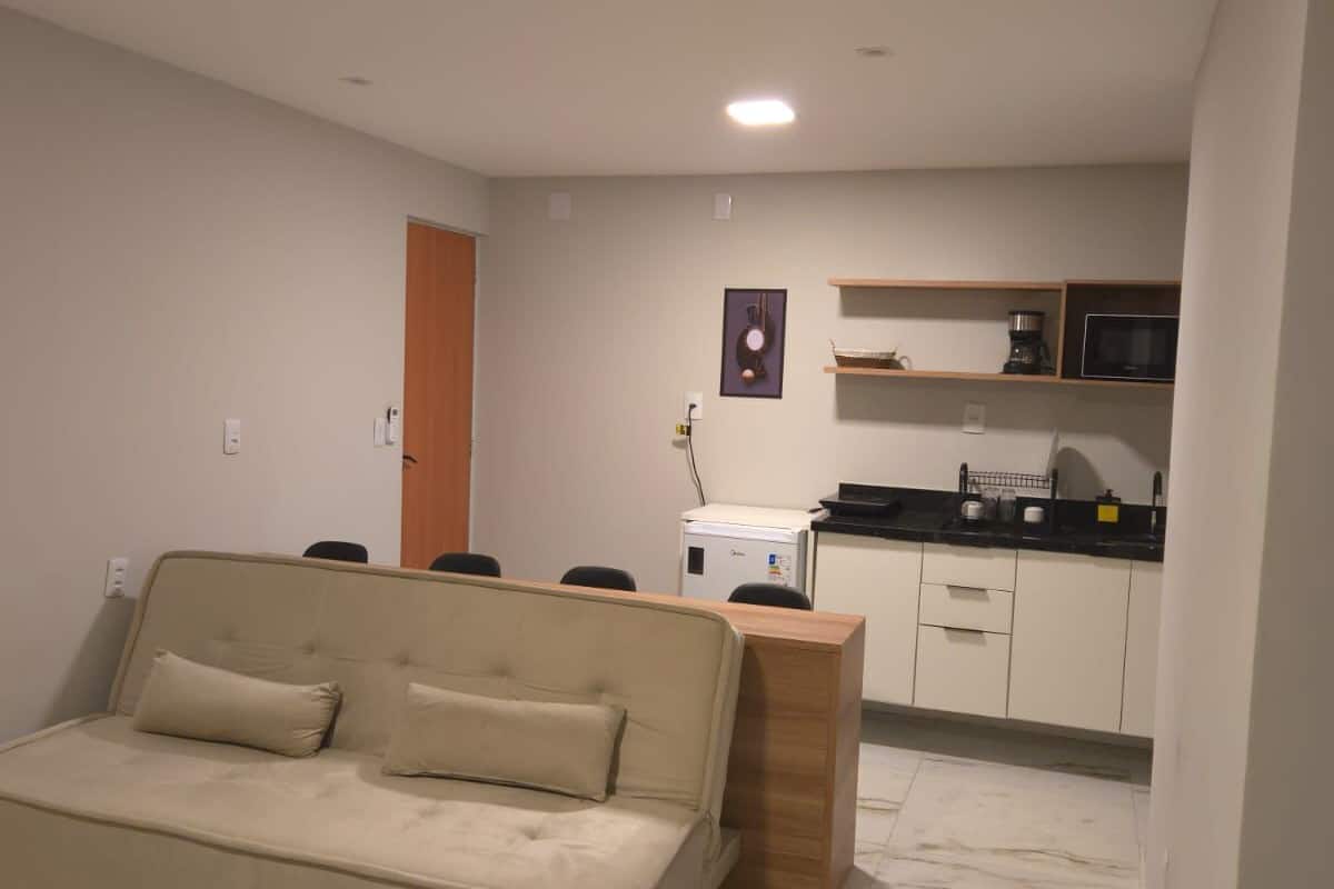 Una sala de estar moderna con un sofá y una mesa de centro de madera, una zona de cocina con un microondas y un fregadero, y un armario pequeño.