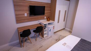 Una habitación compacta con cama, escritorio con dos sillas, televisor y armario.