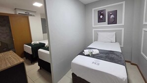 A hotel room with a bed, a desk, a chair, a mirror, and a wall-mounted air conditioner. - M3 Studio Hotel by Concavus (Camacari)