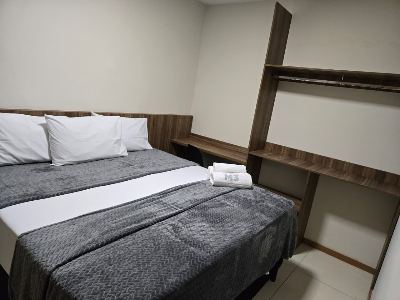 A hotel room with a bed, two pillows, a white towel, and a wooden headboard.