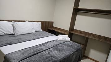 A hotel room with a bed, two pillows, a white towel, and a wooden headboard.