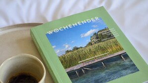 A book titled "WOCHENENDER" with a scenic cover image of a bridge over water, placed next to a cup of coffee on a tray. - Double room in the Gasthaus am Finowkanal (former school from 1875). (Wandlitz)