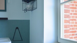 A bathroom with a white sink, a green-tiled wall, a black triangular towel rack, and a window with a brick wall view. - Double room in the Gasthaus am Finowkanal (former school from 1875). (Wandlitz)