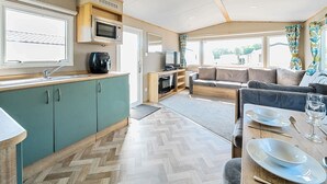 A compact RV interior with a kitchenette, seating area, and large windows. - Dune Delight - Hayling Island (Hayling Island)