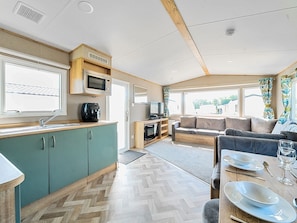 Interior compacto de una caravana con kitchenette, zona de estar y ventanas amplias.