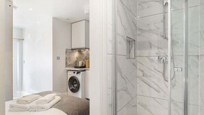 Une chambre d’hôtel moderne équipée d’un lit, d’un lave-linge et d’une cabine de douche en verre.