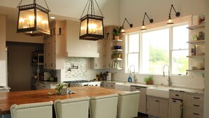 Een moderne keuken met een centraal eiland, hanglampen en een groot raam dat voor natuurlijk licht zorgt.