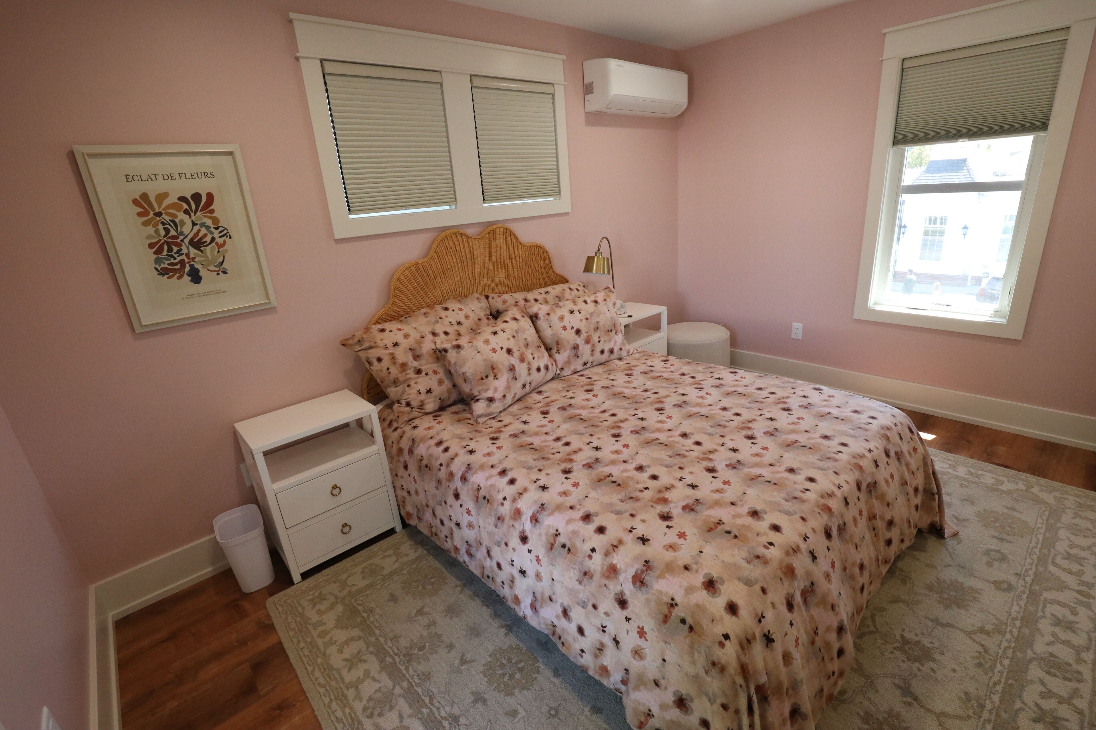 A bedroom with a floral bedspread, a nightstand, a bedside table, and a framed picture on the wall.