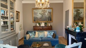 A living room with a blue sofa, a chandelier, a fireplace, and a bookshelf. - Your cosy, quiet suite in the heart of Carcassonne! (Carcassonne)