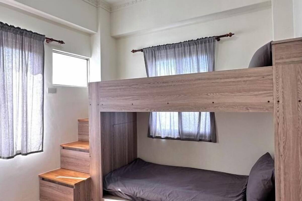 Habitación con literas de madera, una ventana con cortinas y una escalera.