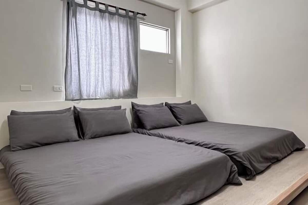 Un dormitorio con dos camas individuales, una ventana con cortina y una mesita de noche pequeña.