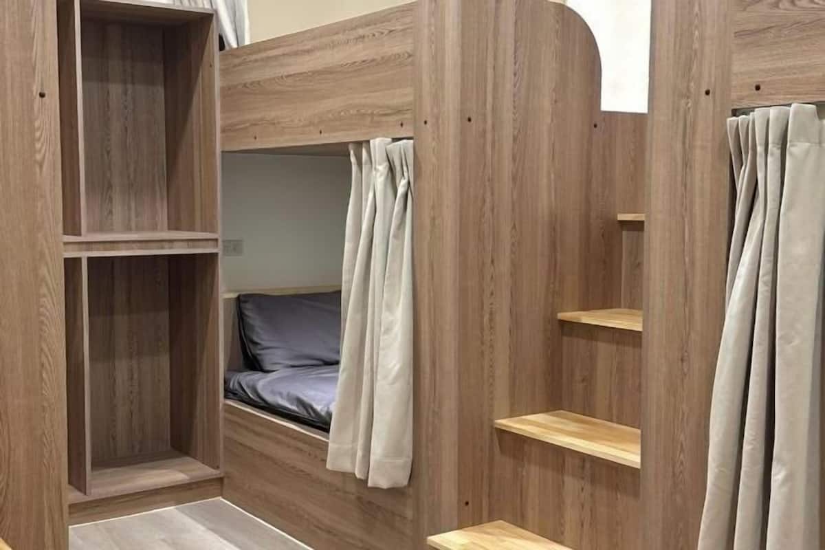 Una cama litera con acabados de madera, un estante pequeño y una cortina.