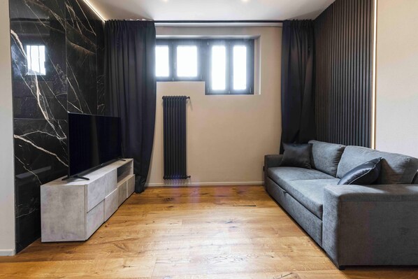 A modern living room with a marble wall, a flat-screen TV, a grey sofa, and a wooden floor.