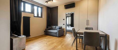 A modern living room with a sofa, a dining table with chairs, a TV, and a radiator.