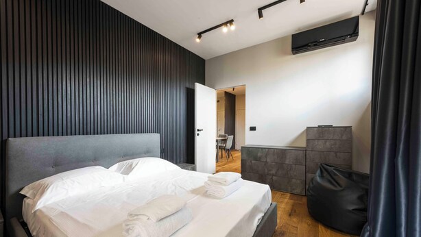 A modern hotel room with a large bed, a grey headboard, a flat-screen TV mounted on the wall, and a wooden floor. - Gozzoli by MMega (Florence)