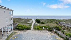 A beachfront property with a sandy path leading to the ocean, a wooden deck, and a building with a balcony. - Contemporary and Relaxing Getaway - 10 minute walk to the beach (Oak Island)