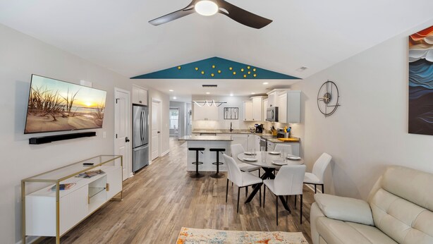 A modern kitchen with white cabinets, a central island, and a dining area with white chairs and a table. - Contemporary and Relaxing Getaway - 10 minute walk to the beach (Oak Island)