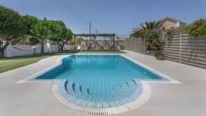 A rectangular swimming pool with a tiled deck, surrounded by a fence, trees, and a pergola. - Villa 'Anogia  1' with Mountain View, Wi-Fi and Air Conditioning (Laganas)