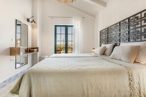 A bedroom with a large bed, a mirror, a wall-mounted shelf, a window with curtains, and a decorative panel. - Villa 'Anogia  1' with Mountain View, Wi-Fi and Air Conditioning (Laganas)