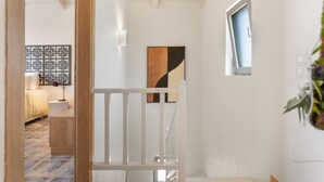 A hallway with a white railing, a door leading to a bedroom, a wall-mounted artwork, and a window with a view. - Villa 'Anogia  1' with Mountain View, Wi-Fi and Air Conditioning (Laganas)
