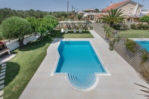 Una piscina rettangolare con bordo piastrellato, circondata da un prato, un pontile in legno e una zona relax coperta.