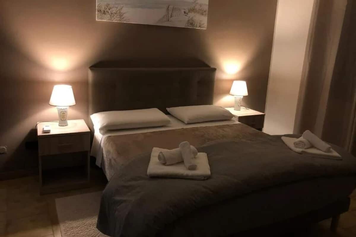 A bedroom with a bed, two bedside lamps, a nightstand, and a painting on the wall.
