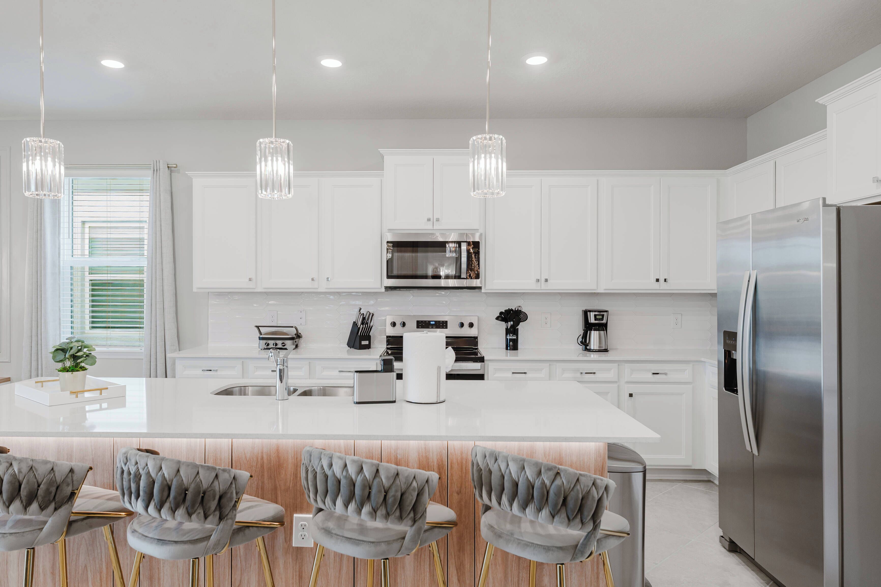 A modern kitchen with white cabinetry, stainless steel appliances, and a central island with bar stools.