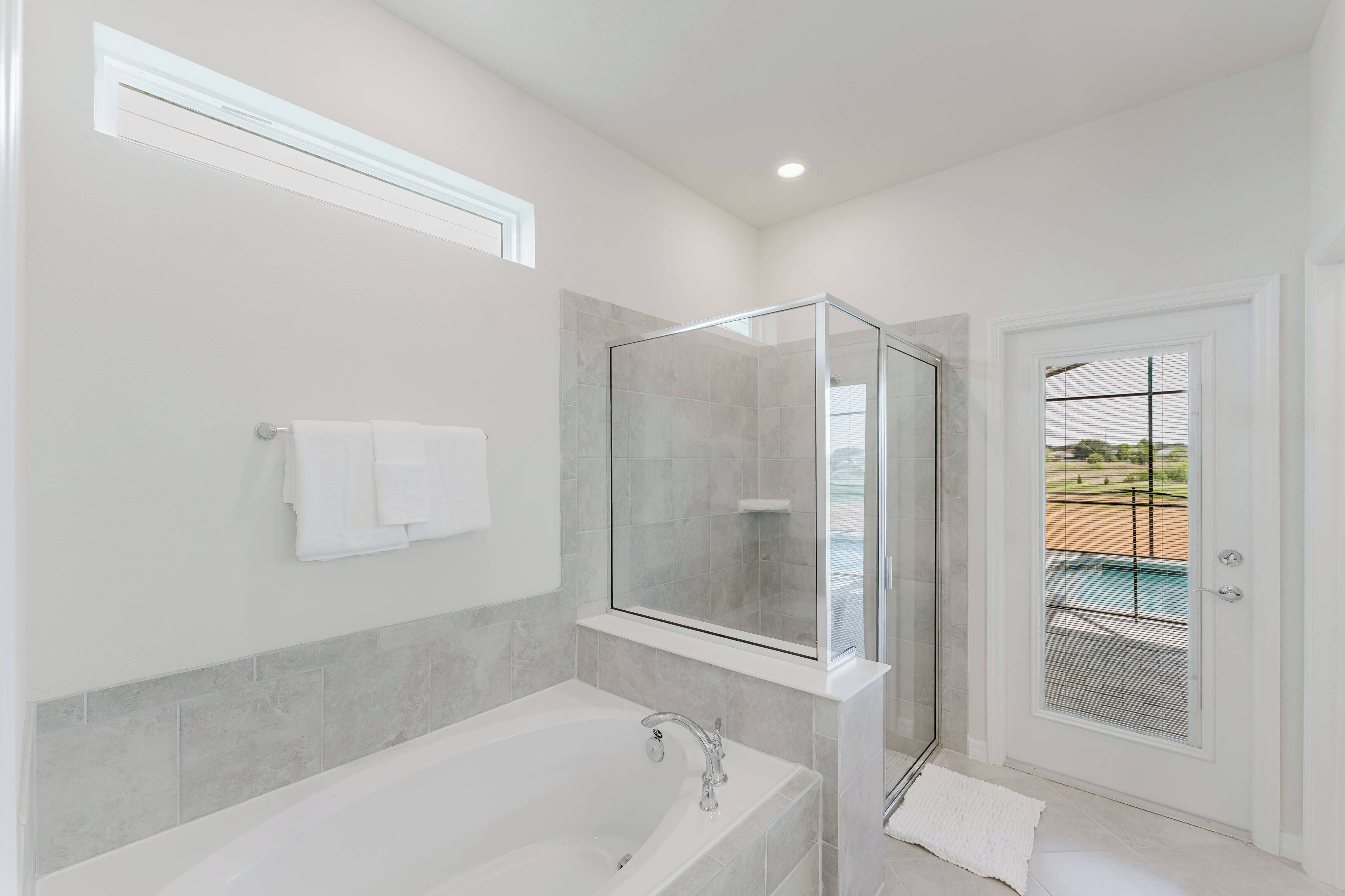 Uma casa de banho moderna com cabine de duche em vidro, banheira e vista para uma piscina através de uma porta.