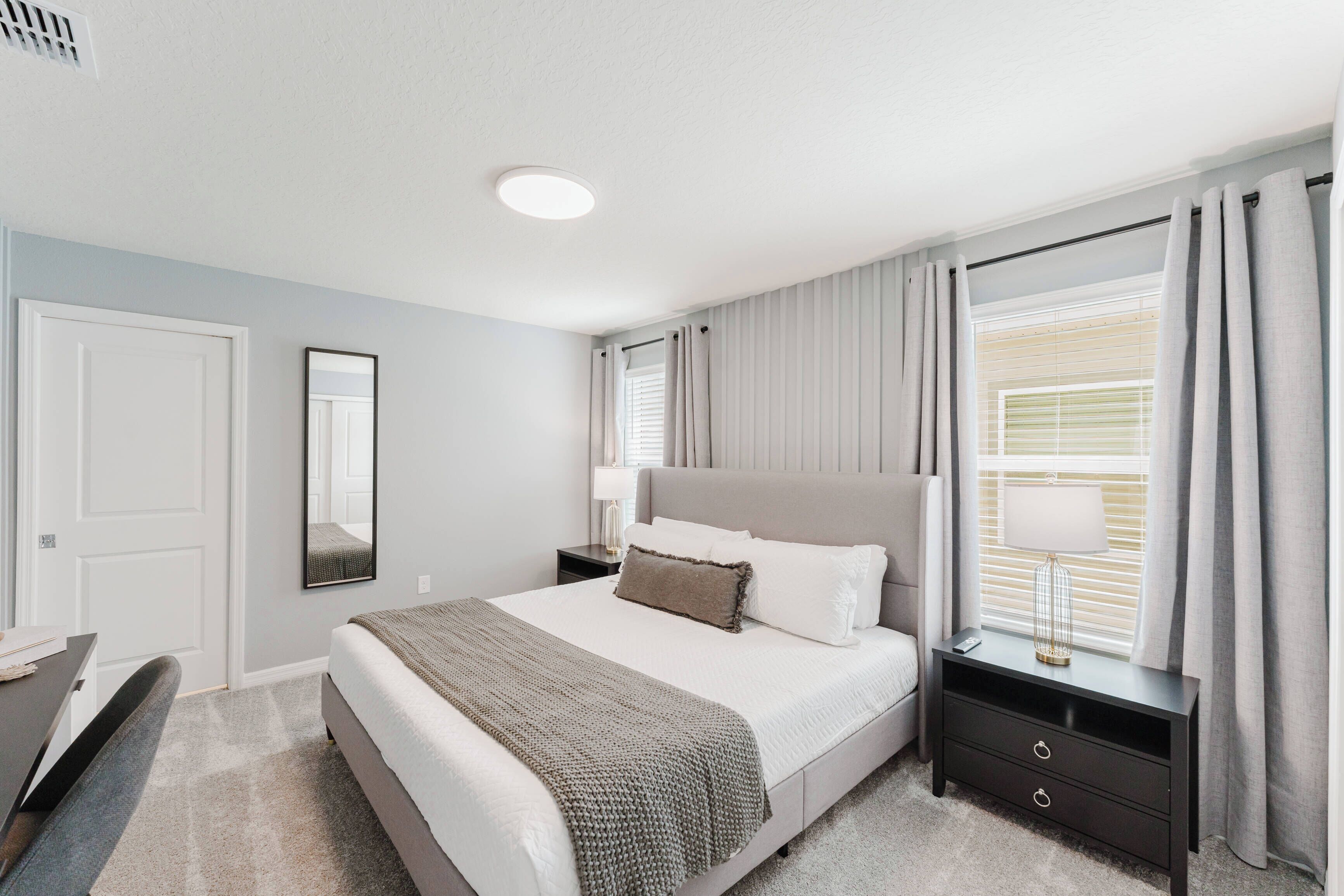 Une chambre à coucher avec un lit, des tables de chevet, une commode, une lampe et une fenêtre avec des rideaux.