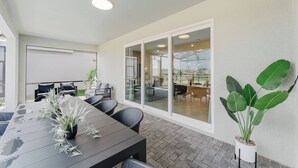 A modern outdoor dining area with a long table, chairs, and potted plants. - Stunning 8BR Pool Gameroom Minutes to Disney (Clermont)