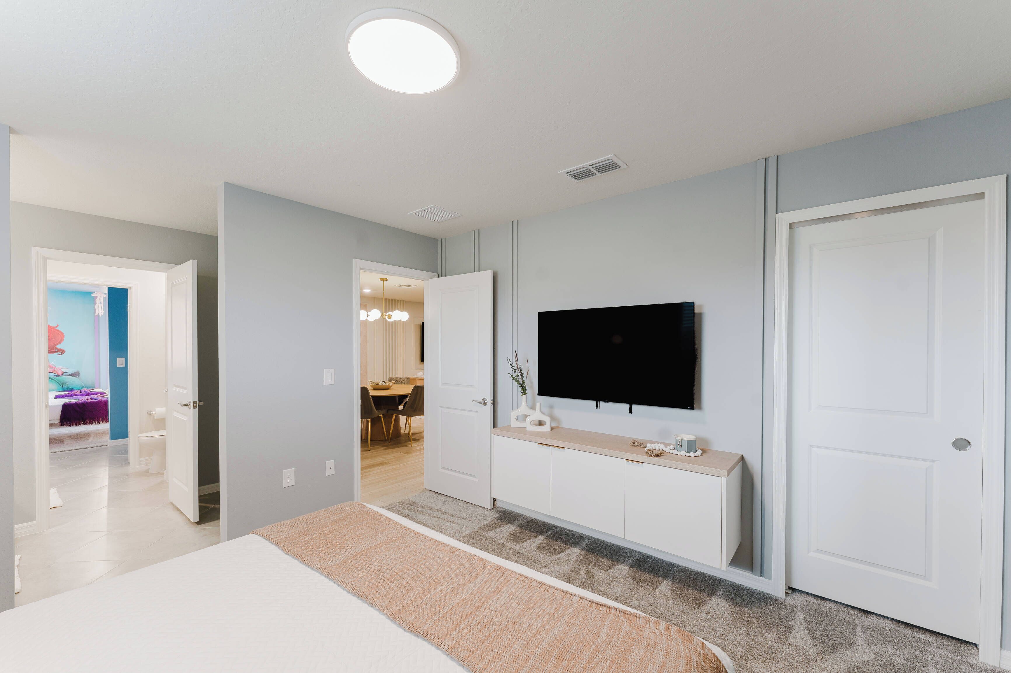Une chambre moderne avec un grand lit, un téléviseur fixé au mur et une porte donnant sur un coin repas.