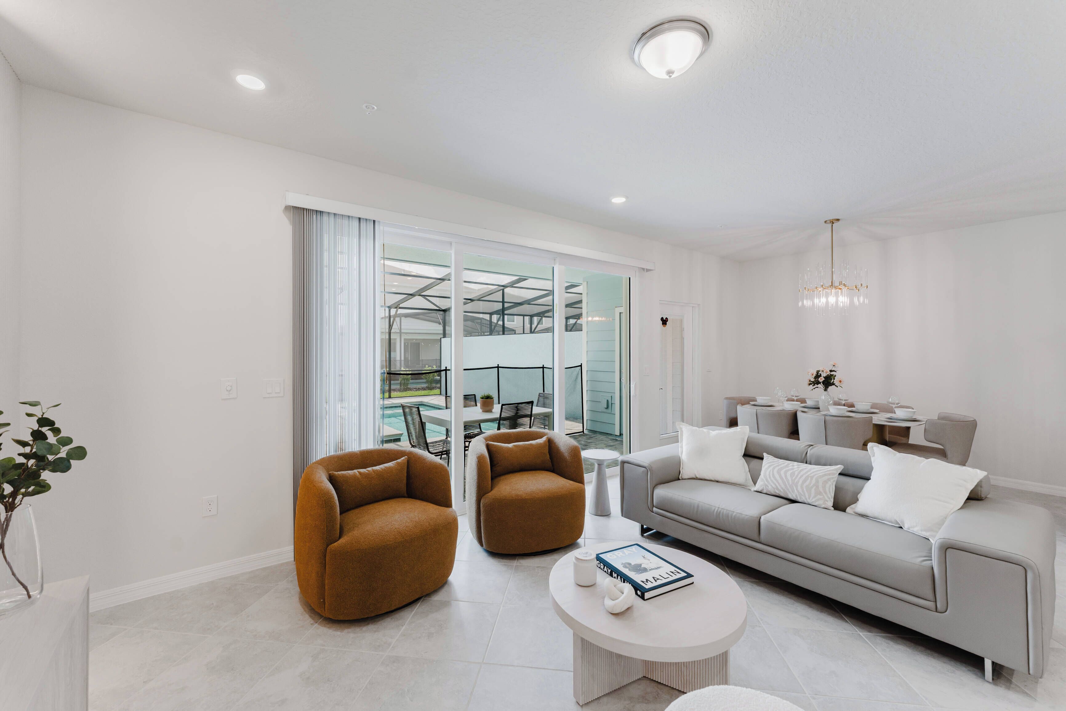 A modern living room with a grey sofa, two brown armchairs, a coffee table, and a chandelier.