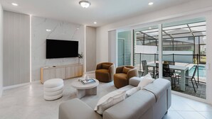 Una sala de estar moderna con una televisión de pantalla plana, un sofá, una mesa de centro y un comedor con vistas a la piscina.