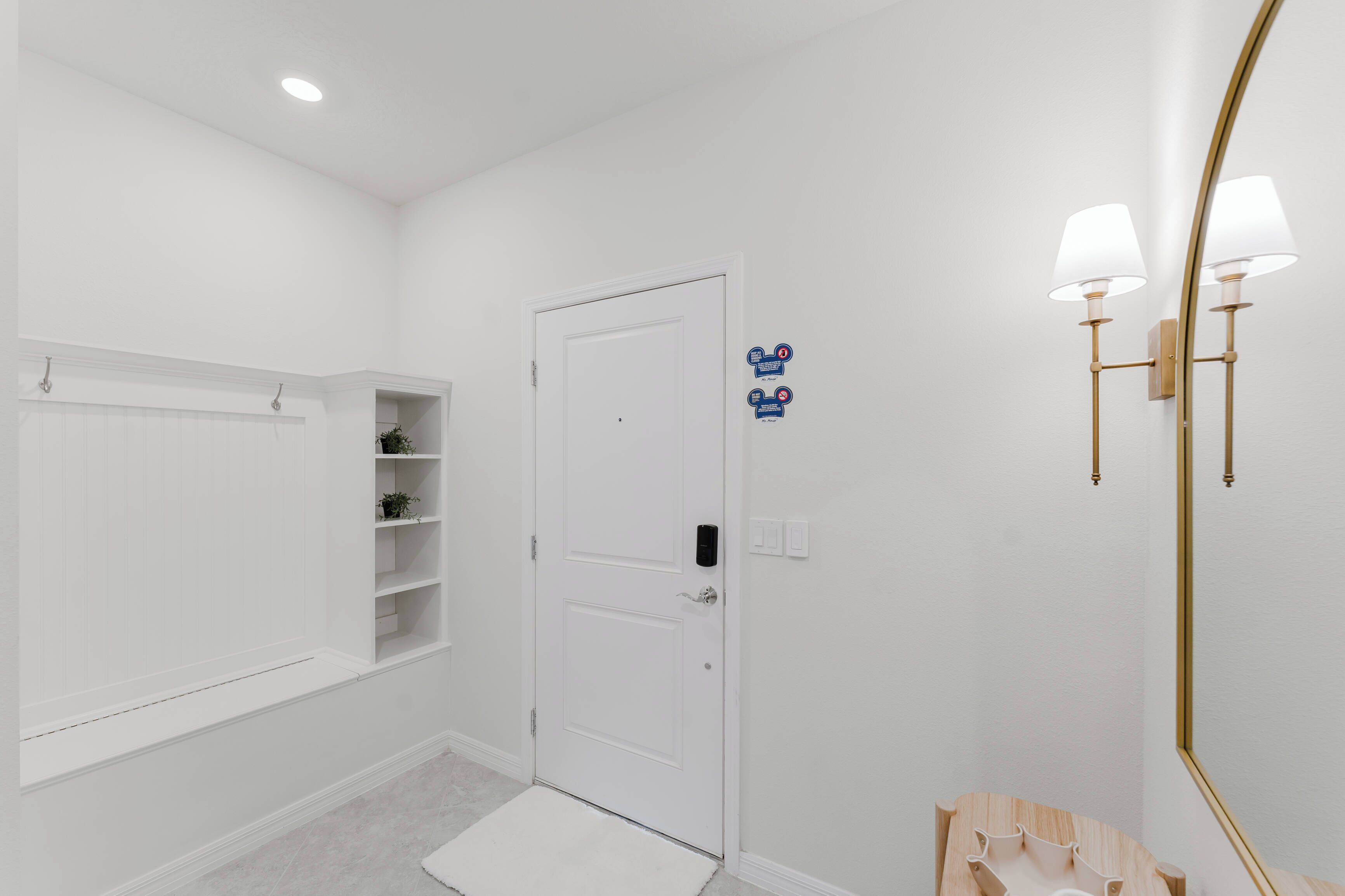 Une salle de bain blanche avec une porte, des étagères, un miroir et un luminaire.