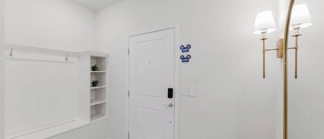 Une salle de bain blanche avec une porte, des étagères, un miroir et un luminaire.