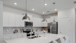 Una cocina moderna con armarios blancos, electrodomésticos de acero inoxidable e iluminación colgante.