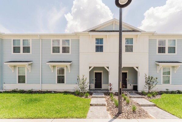 A two-story residential building with a symmetrical facade, a central entrance with a dark door, and a small porch area. - Windsor Cay 5bd With Pool (Clermont)