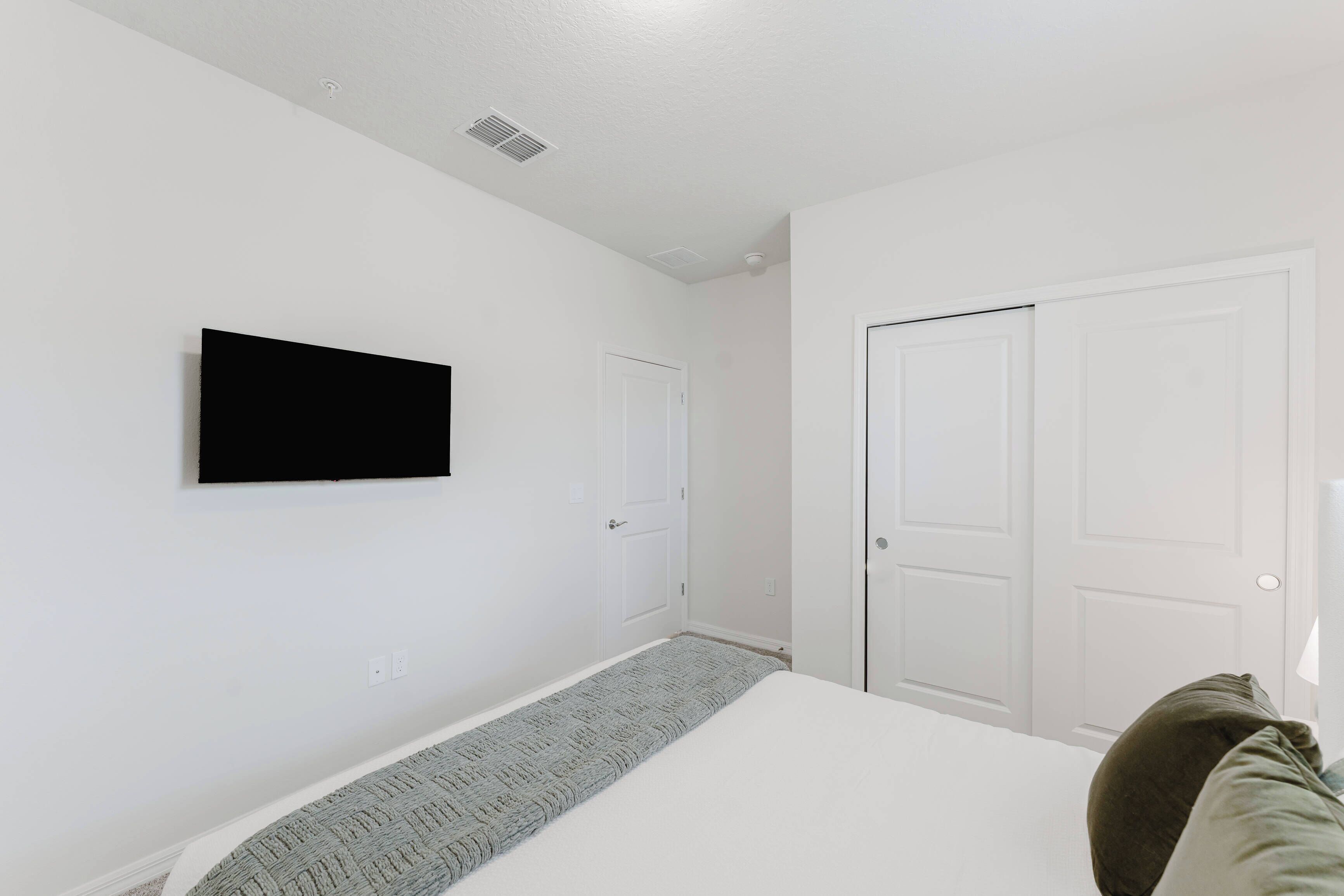 Ein Schlafzimmer mit einem Bett, einem an der Wand montierten Fernseher und zwei weißen Türen.