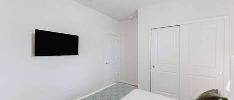 Ein Schlafzimmer mit einem Bett, einem an der Wand montierten Fernseher und zwei weißen Türen.
