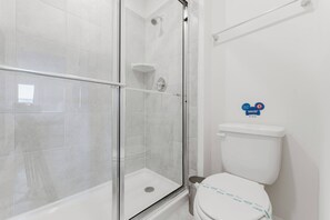 A modern bathroom with a glass-enclosed shower, a white toilet, and a hand dryer. - Windsor Cay 5bd With Pool (Clermont)