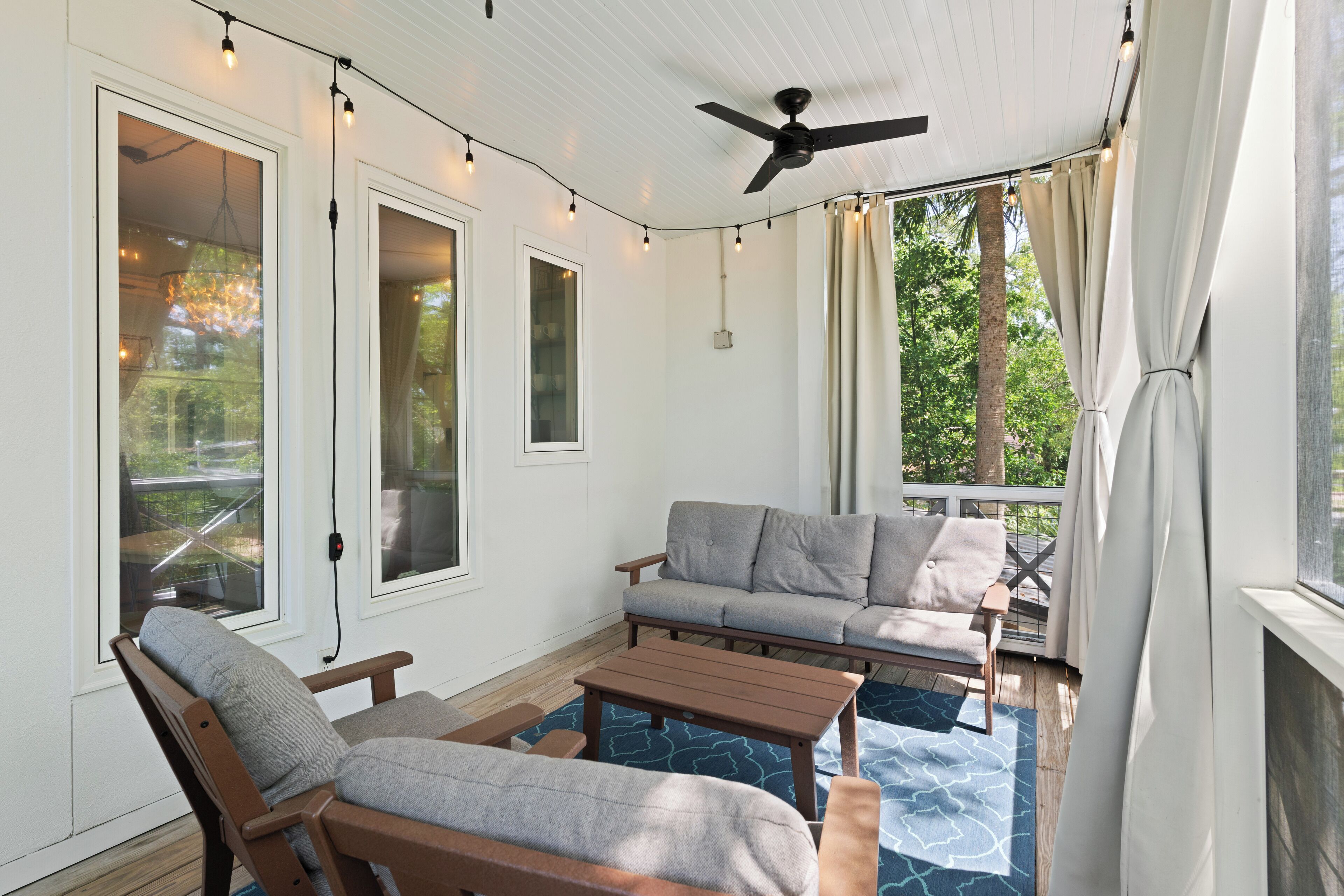 Eine überdachte Terrasse mit Deckenventilator, Lichterketten und einem grauen Sofa.