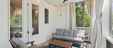 Eine überdachte Terrasse mit Deckenventilator, Lichterketten und einem grauen Sofa.
