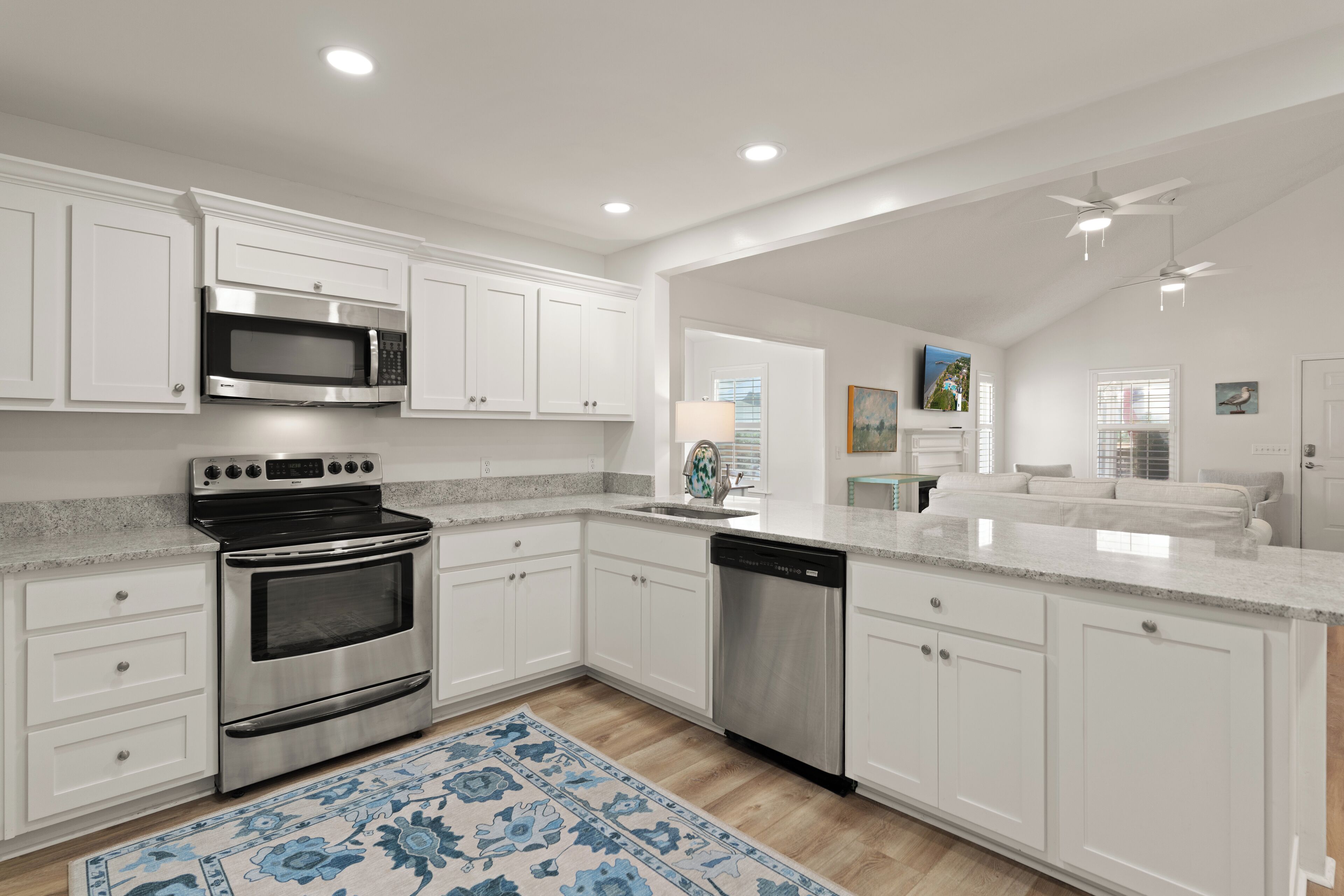 A modern kitchen with white cabinetry, stainless steel appliances, and a blue patterned rug.