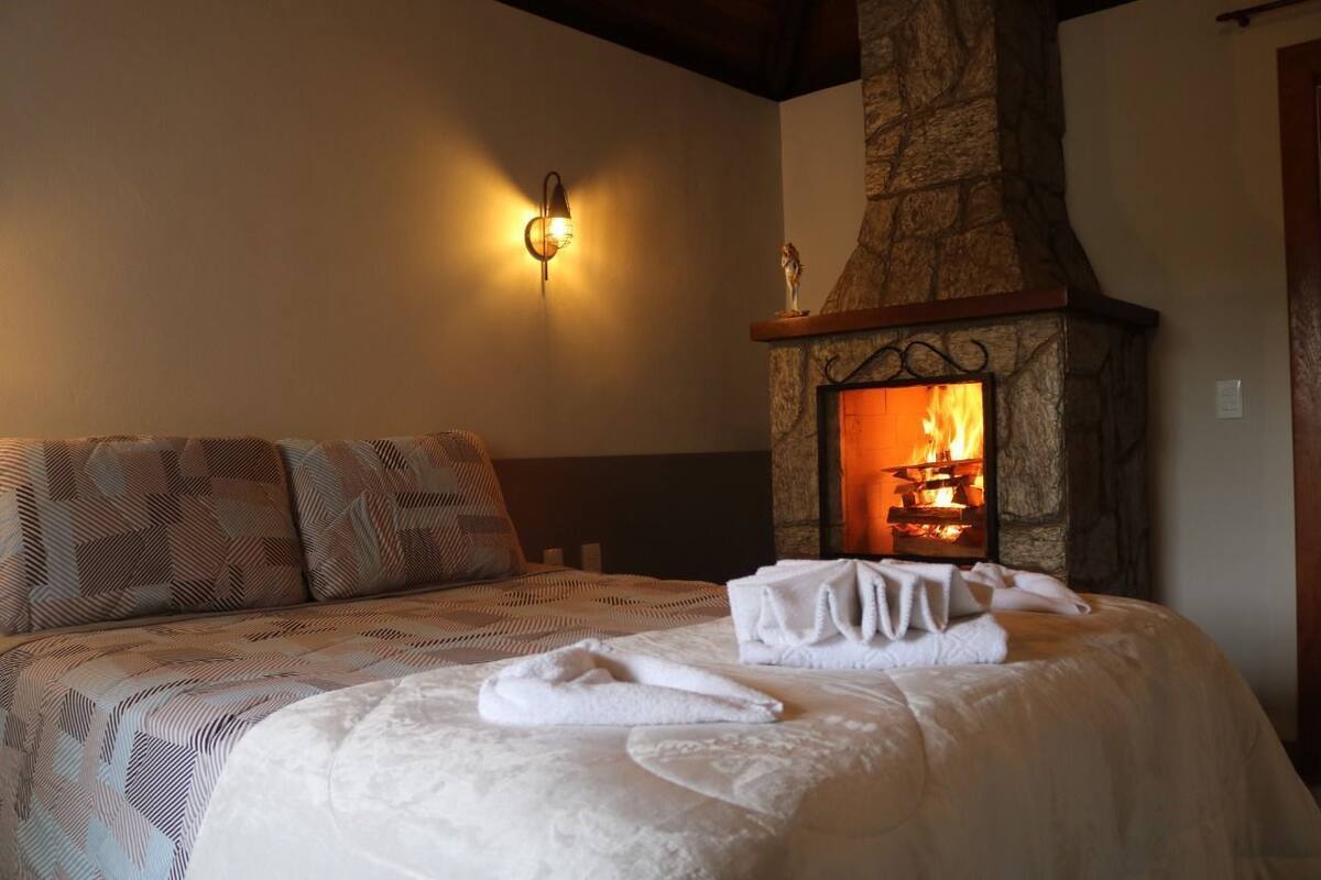 Un dormitorio acogedor con chimenea de piedra, una cama con ropa de cama estampada y una lámpara fijada a la pared.