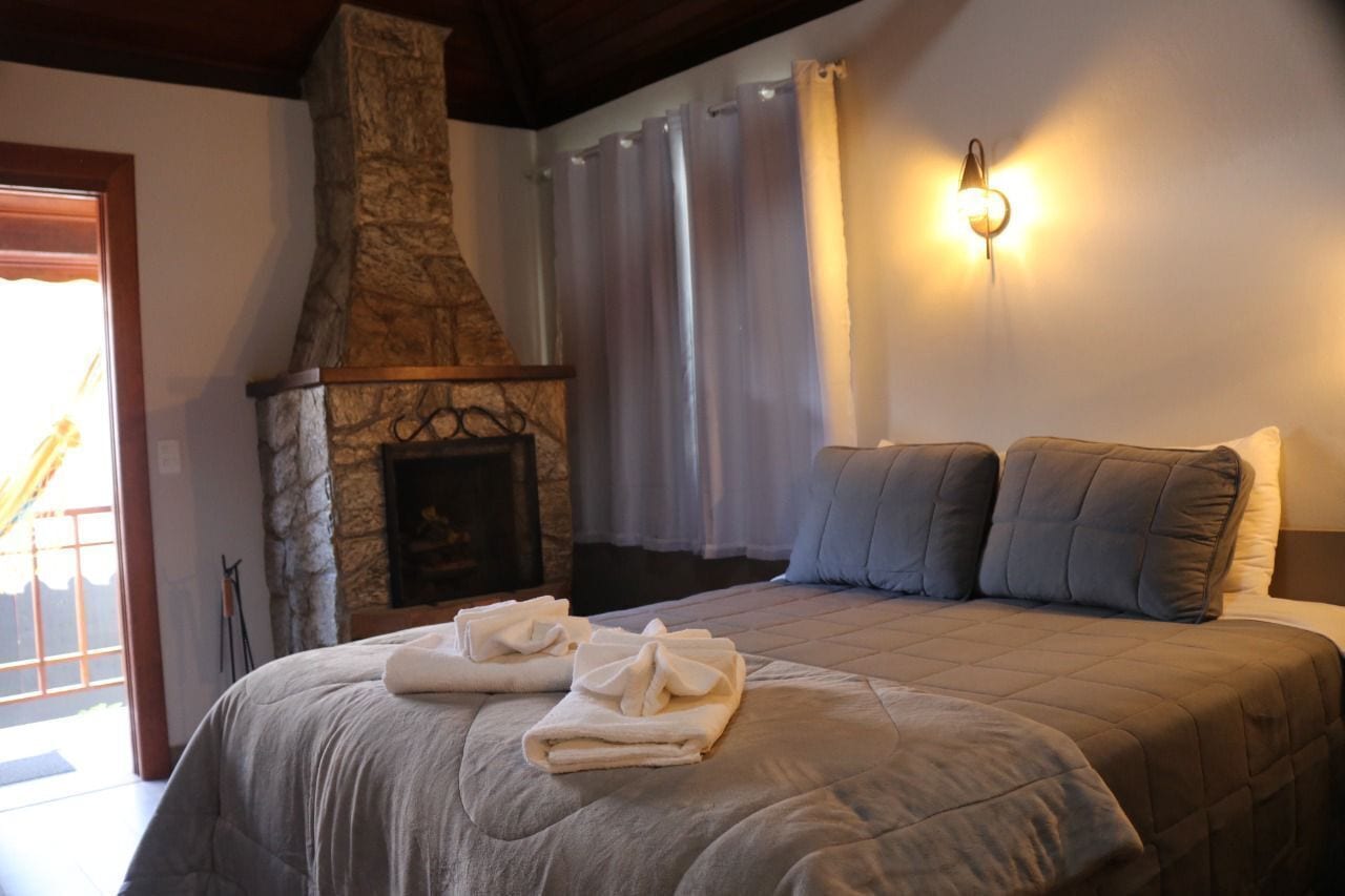 Une chambre avec une cheminée en pierre, un lit recouvert d’une courtepointe matelassée, deux oreillers et un luminaire fixé au mur.