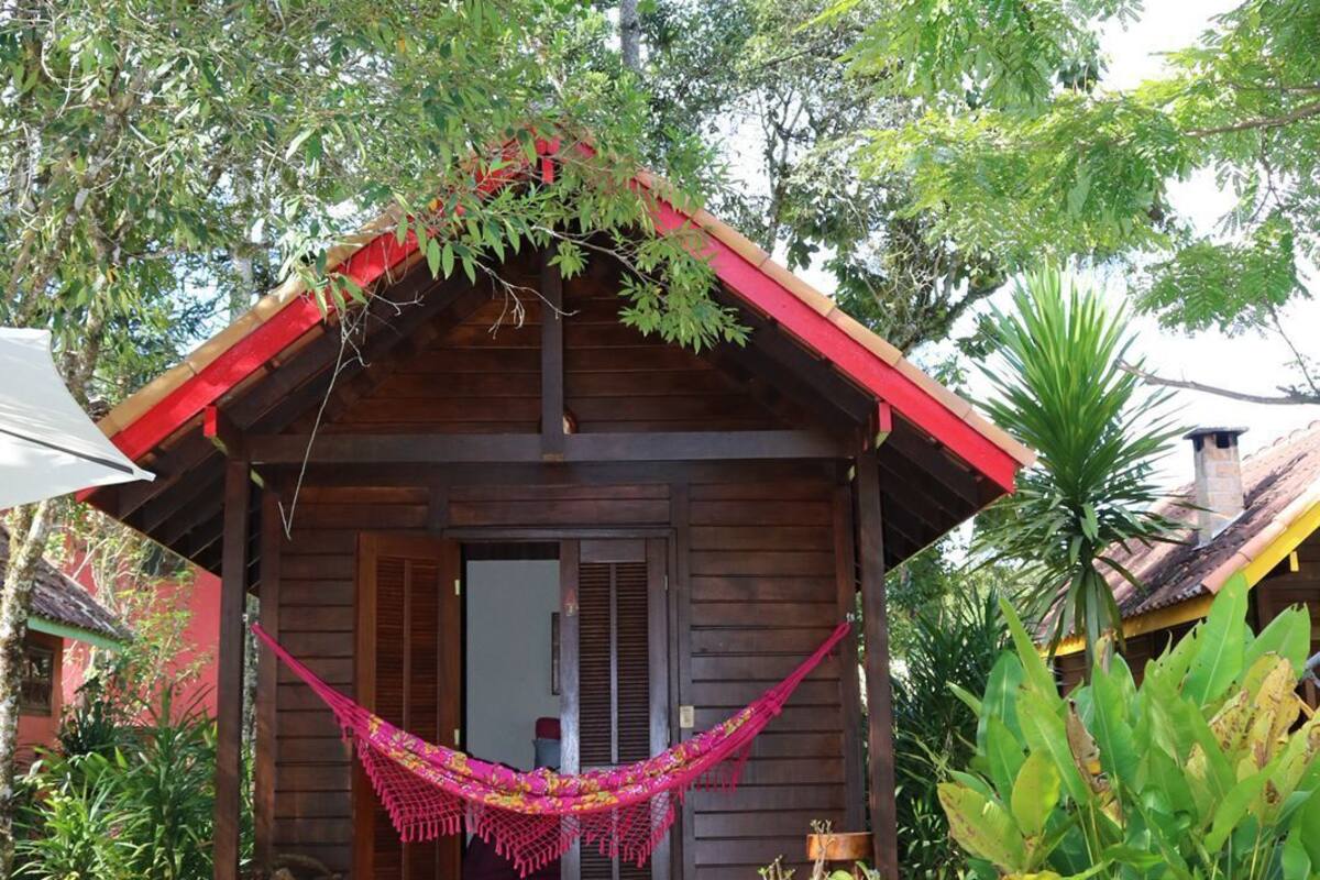 Una cabaña de madera con techo rojo, una hamaca y una escalera de piedra que lleva a la entrada.
