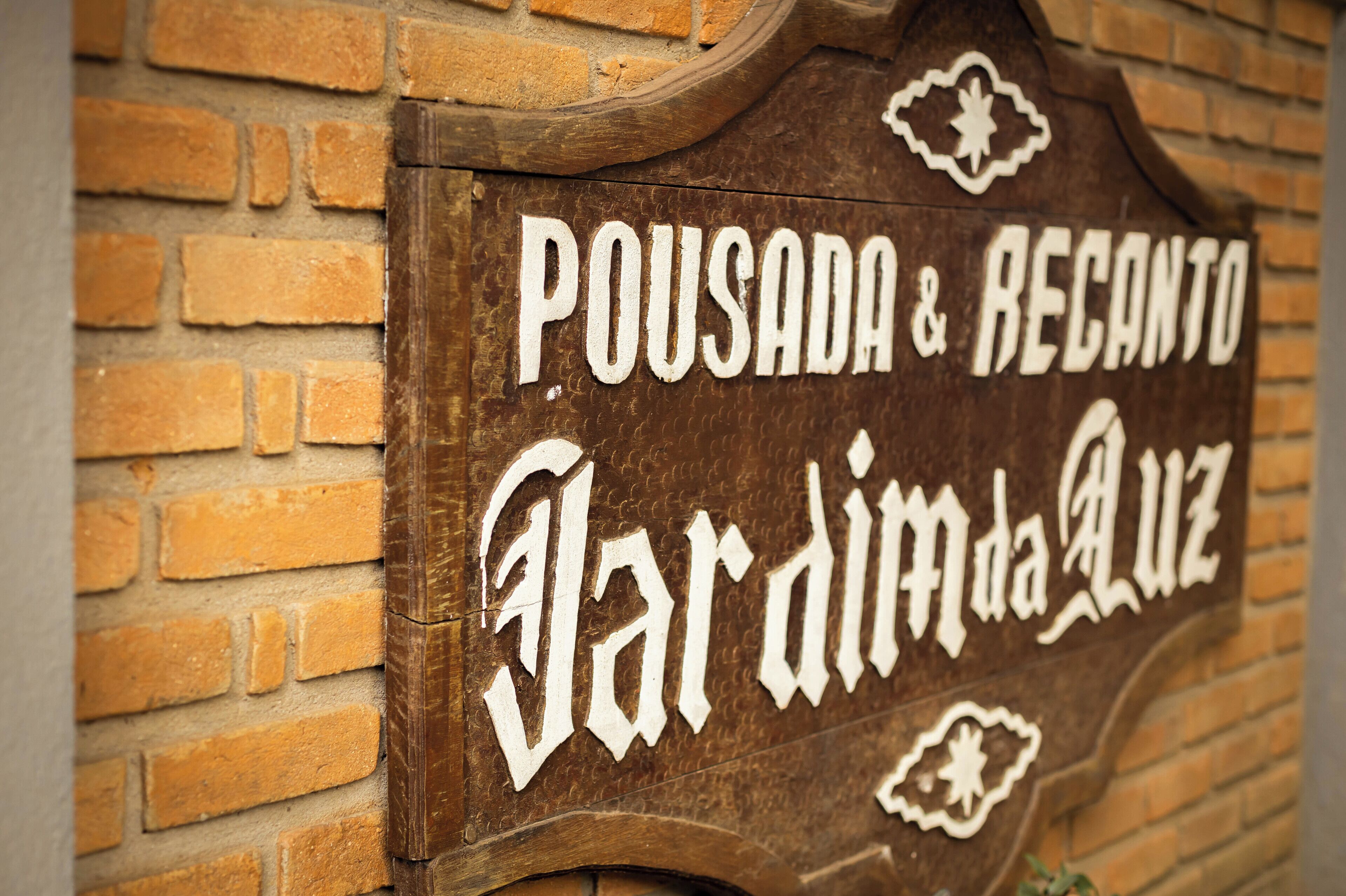 A wooden sign with the text "POUSADA & RECANTO Jardim da Luz".